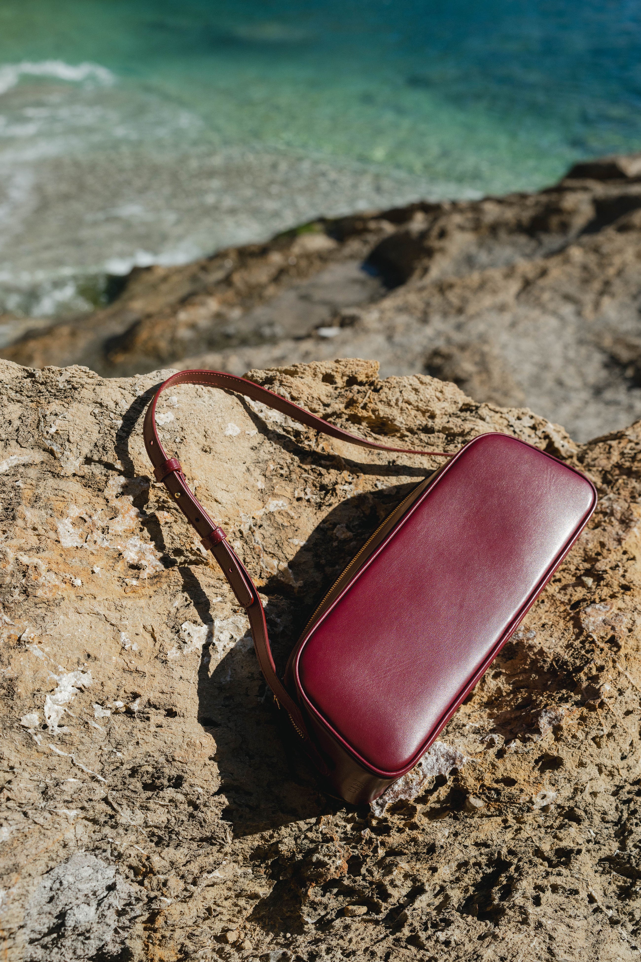 Maroon leather pouch on a rocky surface with ocean in the background