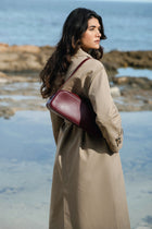 Woman in a beige coat with a burgundy leather bag standing by the water