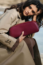 Woman holding a maroon handbag against a blurred natural background