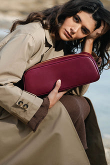 Woman holding a maroon handbag against a blurred natural background