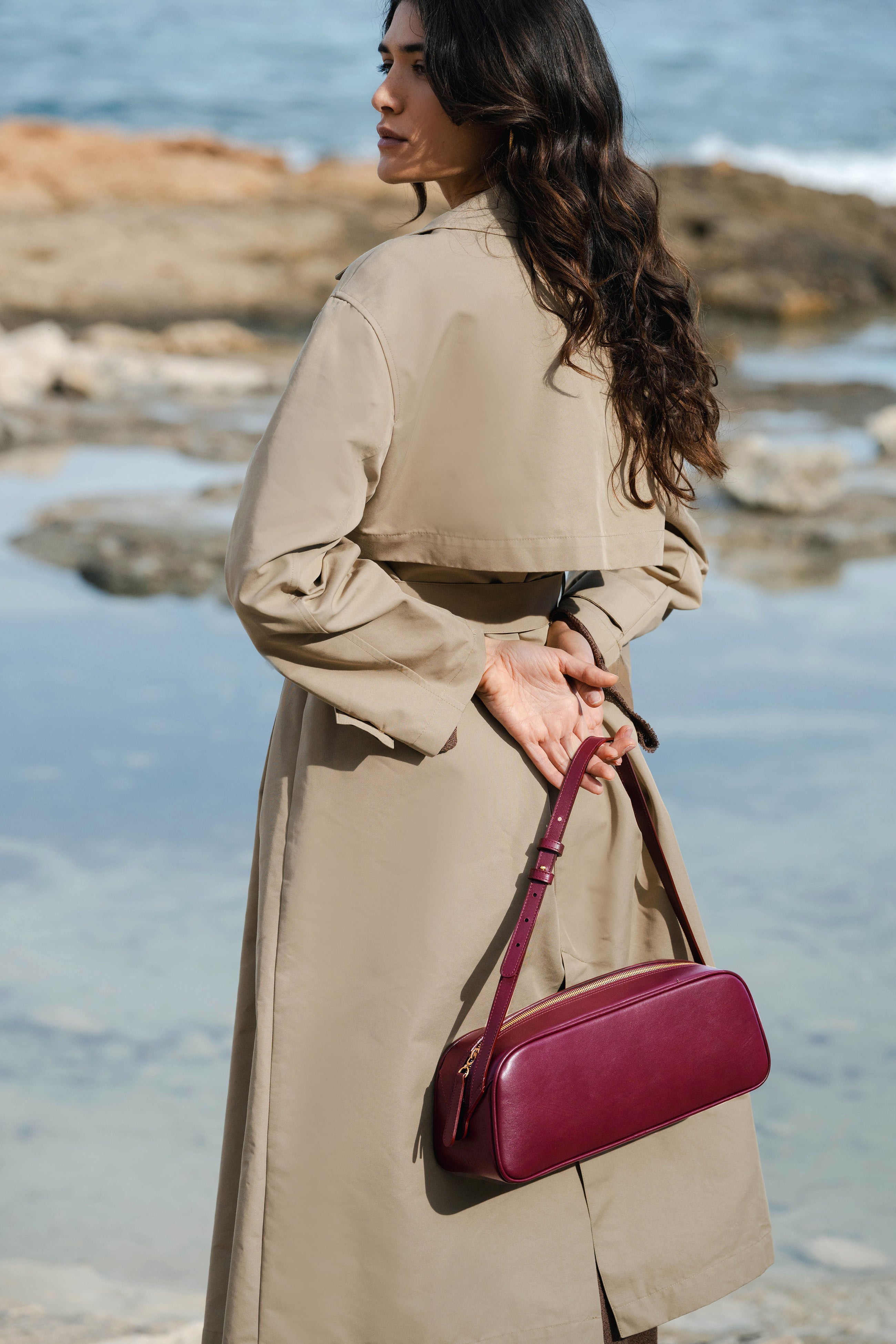 Woman holding a burgundy handbag by the water